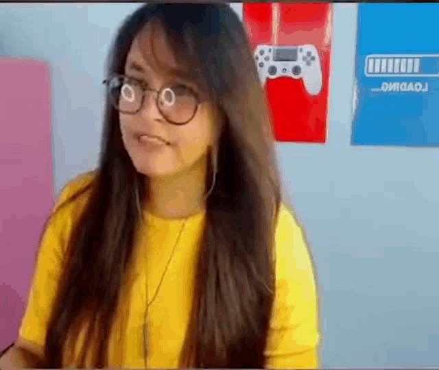 a woman wearing glasses and a yellow shirt is standing in front of a wall with posters on it .