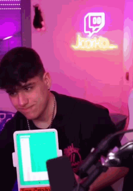 a young man is sitting in front of a microphone in a room with a neon sign that says twitch .