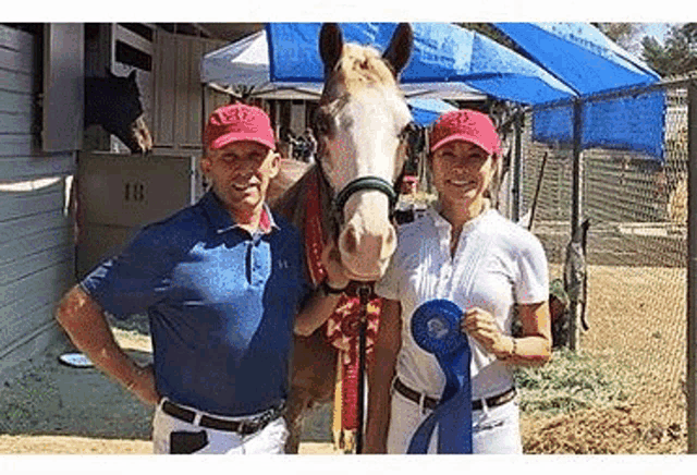 a man and a woman are standing next to a horse holding a blue ribbon .
