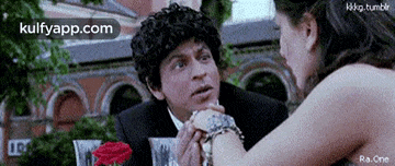 a man in a suit is holding a woman 's hand while they are sitting at a table .