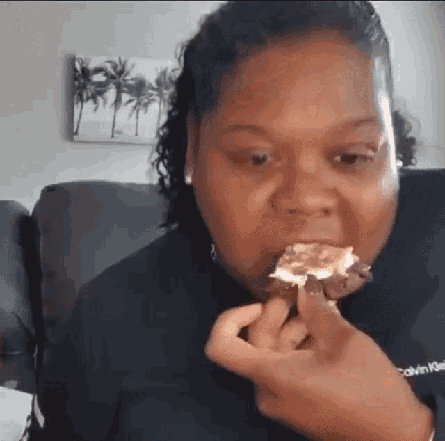 a woman is sitting on a couch eating a cupcake with a bite taken out of it .