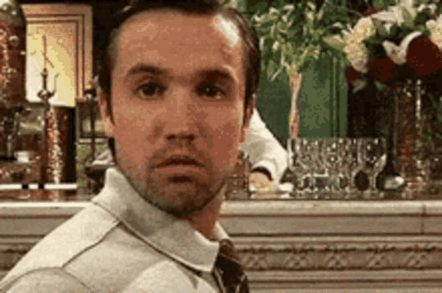 a man in a tie is standing in front of a fireplace