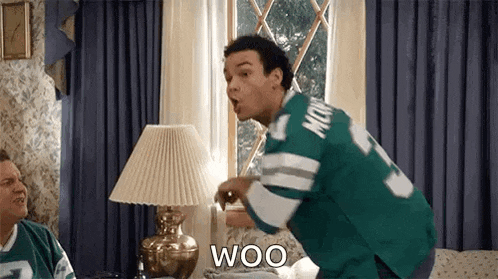 a man in a green jersey is standing in front of a lamp in a living room and shouting .