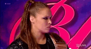 a woman in a black leather jacket is standing in front of a pink and purple background .