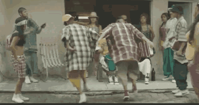 a group of people are dancing in front of a building on the sidewalk .