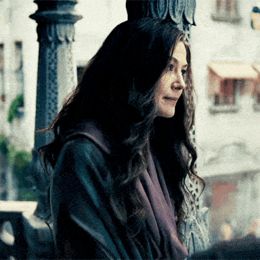a woman with long dark hair is standing in front of a pillar .