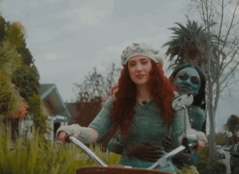 a woman with red hair is riding a bicycle with a doll on the back