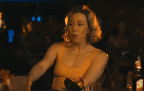 a woman in a yellow tank top is sitting at a table with a bottle of johnnie walker in front of her