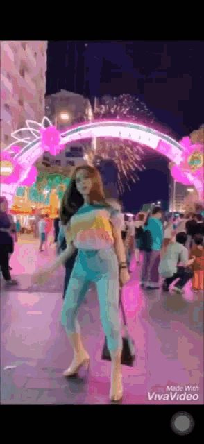 a woman is standing in front of a pink archway with fireworks behind her