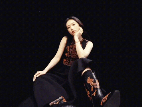 a woman wearing a black dress and cowboy boots is sitting down