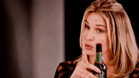 a woman is holding a bottle of wine and making a face .