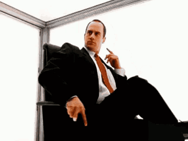 a man in a suit is sitting in a black office chair looking out a window .
