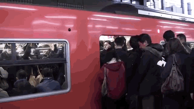a crowd of people getting on a red train at a station