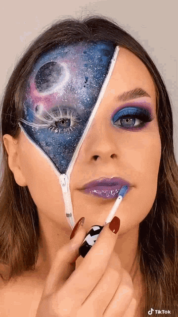 a woman has a galaxy painted on her face and is applying makeup