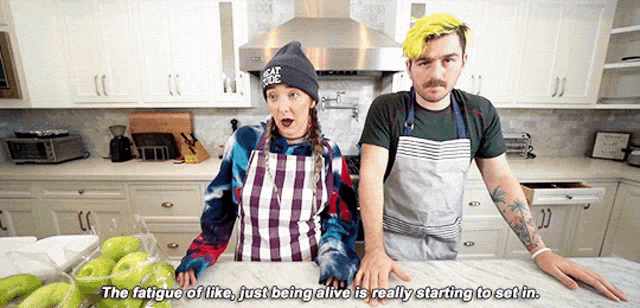 a man and a woman are standing in a kitchen and the woman is wearing a beanie that says dead cells