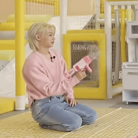 a woman in a pink sweater is kneeling on the floor holding a toy gun