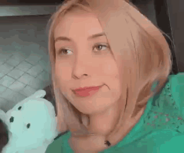 a woman in a green shirt is making a funny face while holding a teddy bear .