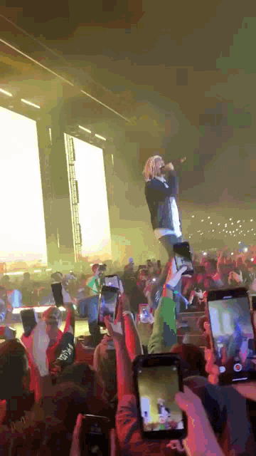 a man stands on a stage with a microphone in front of a crowd that is taking pictures