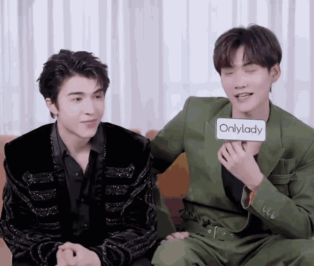 two men are sitting next to each other and one has a sign that says onlylady on it