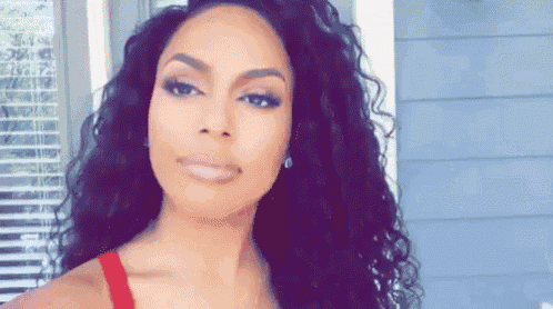 a woman with long curly hair is wearing a red tank top and earrings .