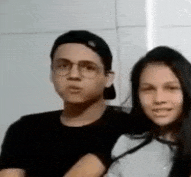 a man and a woman are posing for a picture together . the man is wearing glasses and a hat .