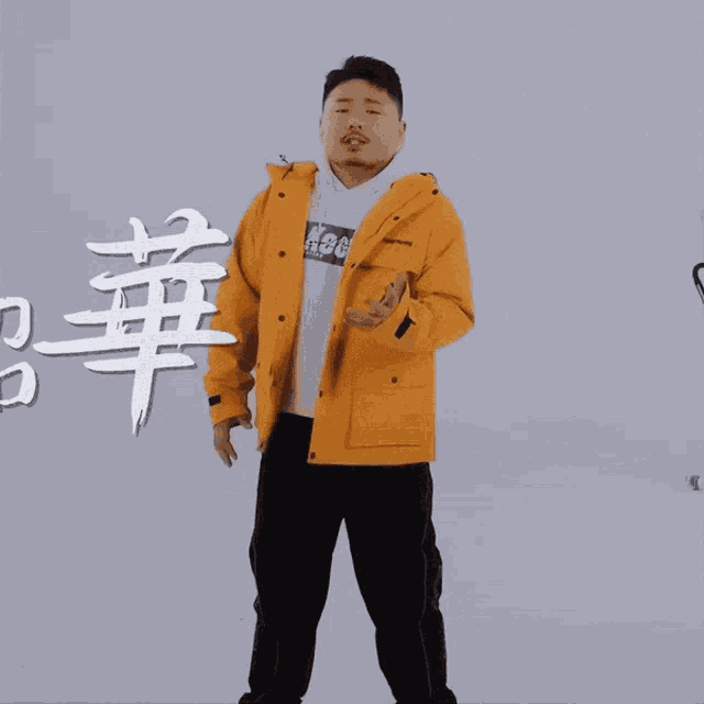 a man wearing a yellow jacket and a white hoodie has chinese writing on the wall behind him