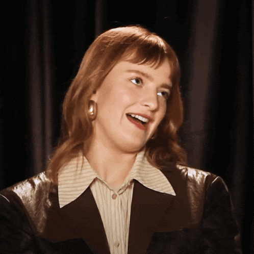 a woman wearing a striped shirt and a black jacket smiles