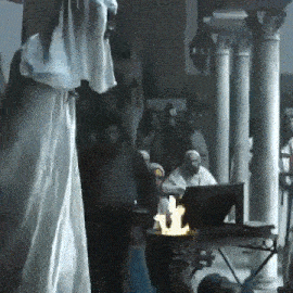 a group of people are standing around a table with a candle on it in a room .