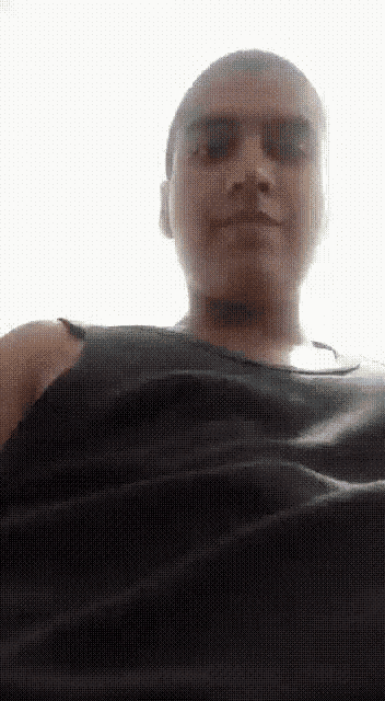 a man with a shaved head wearing a black tank top looks at the camera