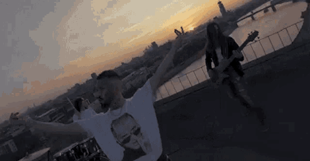 a man is standing on top of a roof with his arms outstretched while a man plays a guitar .