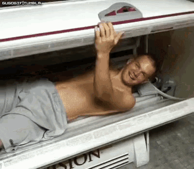 a shirtless man is laying in a tanning bed