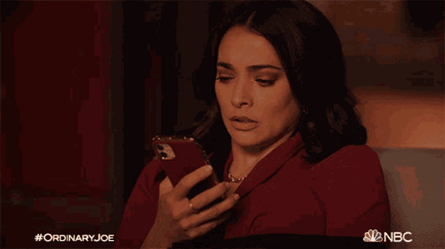 a woman sitting on a couch holding a cell phone with a nbc logo in the background