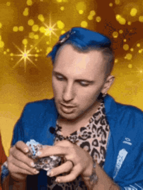 a man with blue hair and a leopard print shirt is holding something in his hands