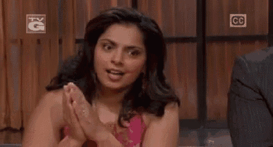 a woman is sitting at a table with her hands folded in front of a tv screen .