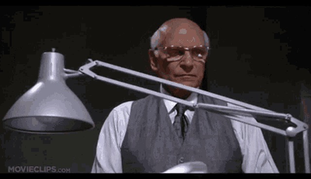 a man with glasses is standing next to a lamp .