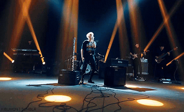a man singing into a microphone on a stage with a band behind him