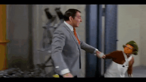 a man in a suit and tie is shaking hands with a cartoon character in overalls .