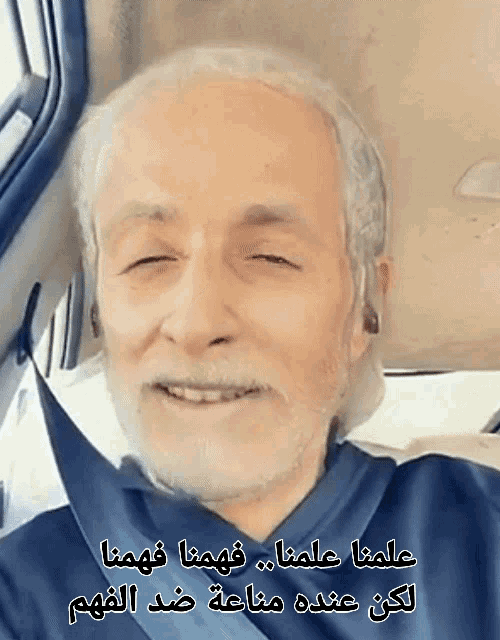 a man with a beard is smiling in a car with arabic writing behind him