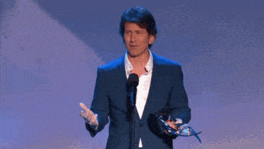 a man in a blue suit stands in front of a microphone holding an award
