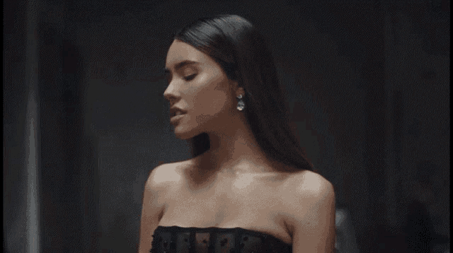 a woman wearing a black strapless dress and earrings looks down