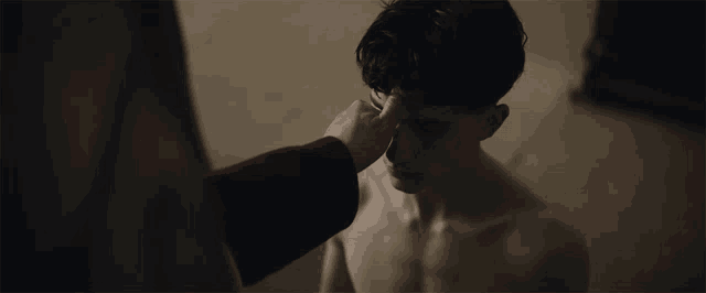 a man without a shirt is being touched by a woman 's hand on his face .