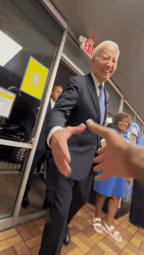 a man in a suit is shaking hands with a woman in a blue dress in front of an exit sign