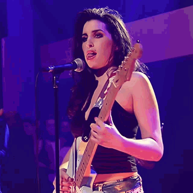 a woman sings into a microphone while holding a guitar