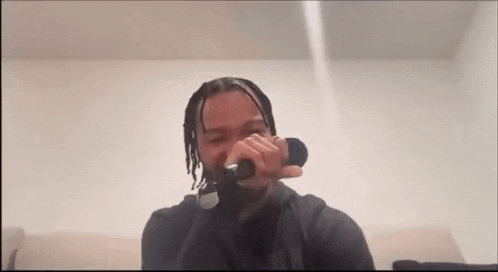 a man is singing into a microphone while sitting on a couch in a room .