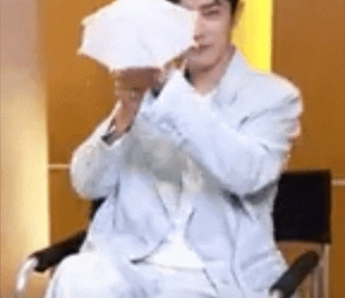 a man in a suit is sitting in a chair holding a white umbrella over his face .