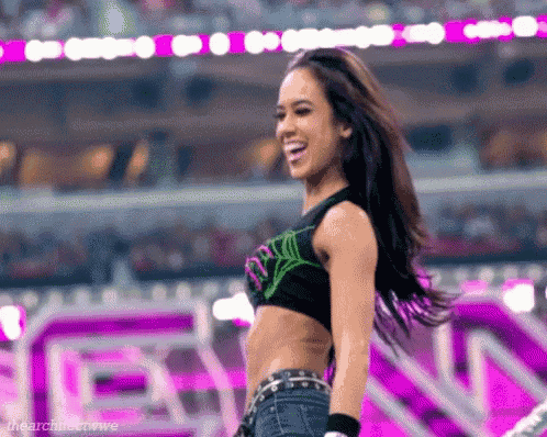 a woman in a crop top and jeans is standing on a stage in front of a crowd and smiling .