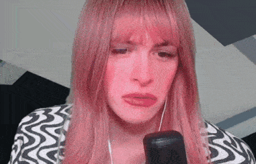 a woman with pink hair is looking at a microphone and making a funny face .