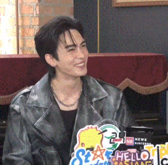 a man wearing a leather jacket is smiling in front of a sign that says hello