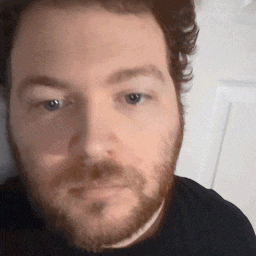a man with a beard wearing a black shirt is looking at the camera