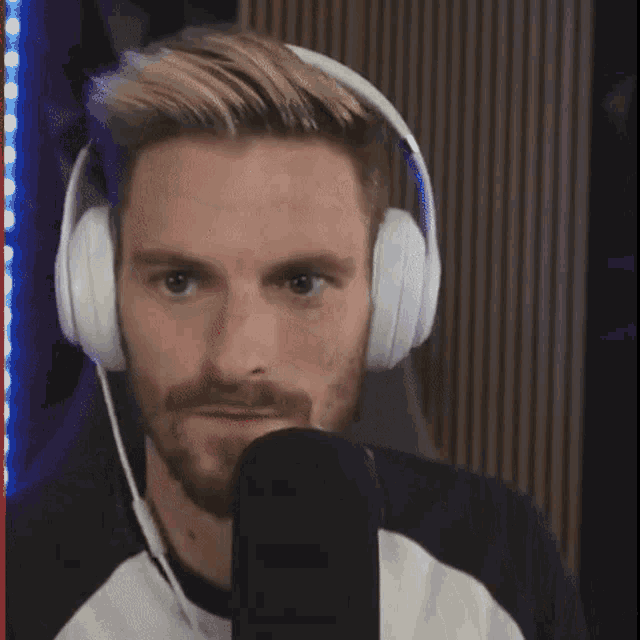 a man with a beard is wearing headphones and looking at a microphone .